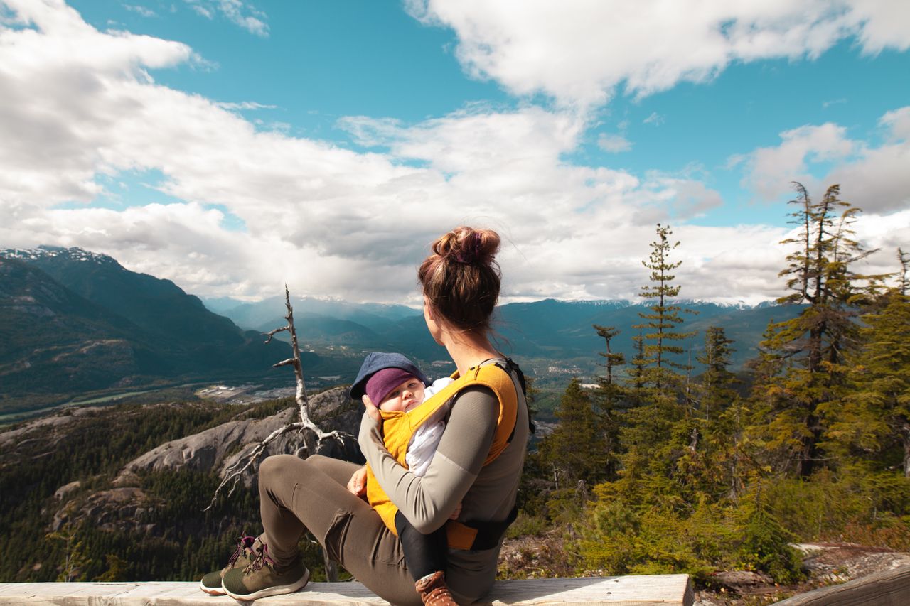 team-02 A mother sits with her baby overlooking a scenic mountain landscape, enjoying nature's beauty.