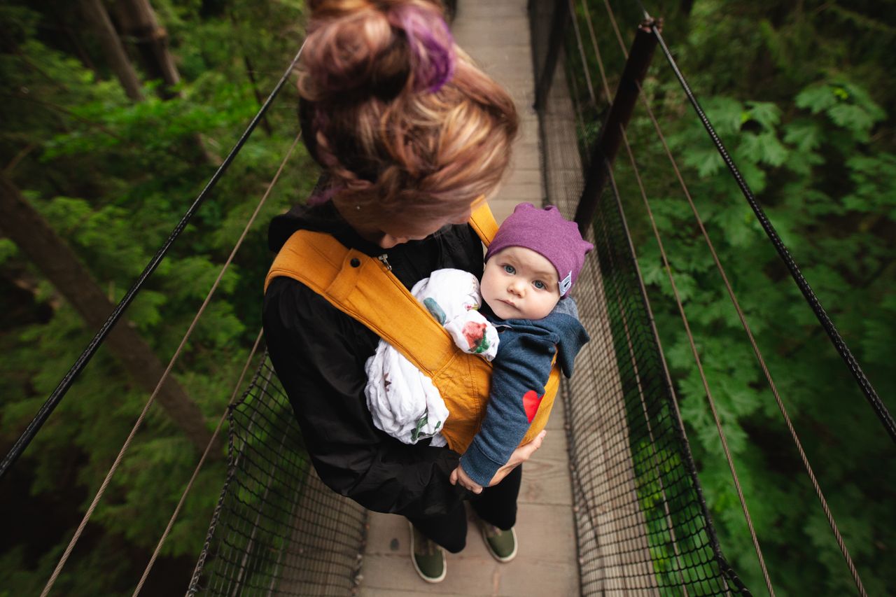 team-01 A woman carries her baby over a forest suspension bridge, highlighting maternal care.