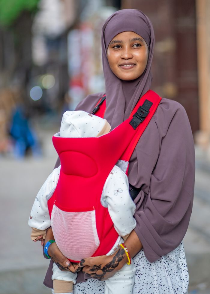 services-02 A smiling Somali mother holds her baby in a red carrier on a street in Mogadishu, Somalia.